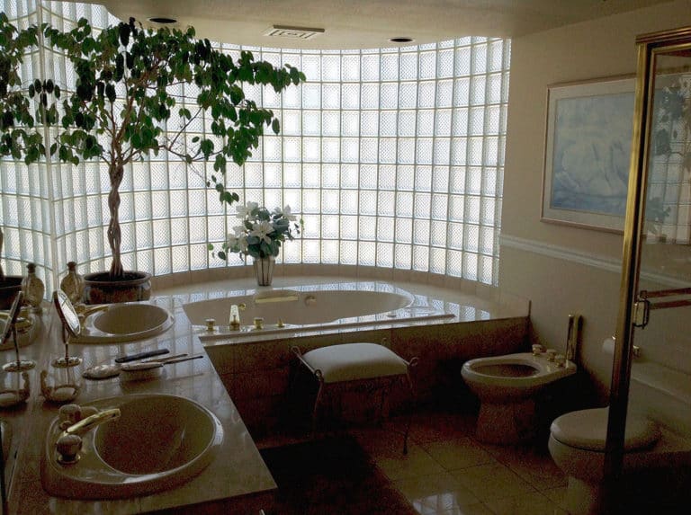 Sailor Retreat before renovation, a glass block wall curving around a drop-in tub and twin basins.