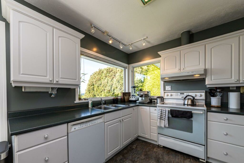 Kitchen before renovation, white raised-panel cabinets and dark green counters under a vaulted ceiling.