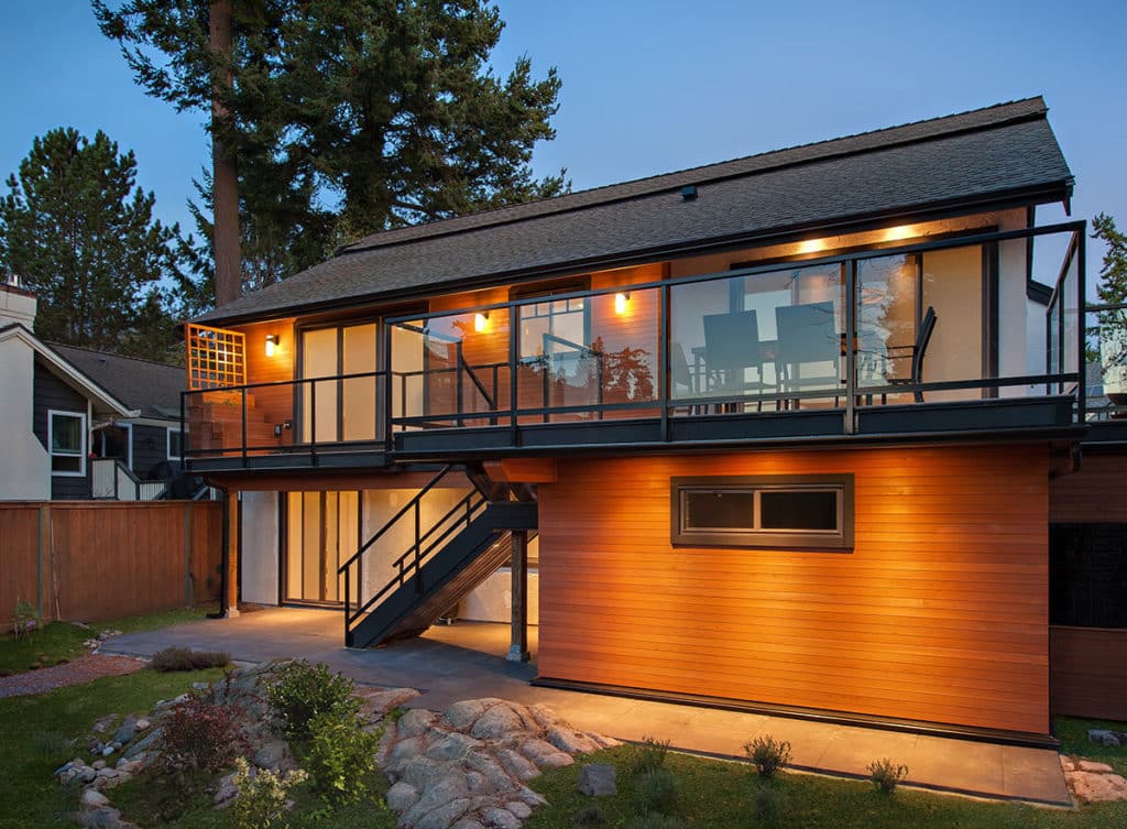 Meadfield after renovation, cedar cladding below a glazed upper storey lit at dusk.