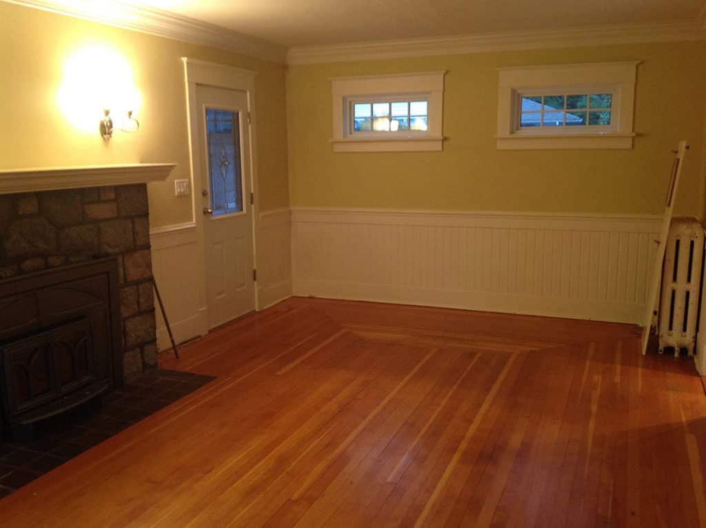 Queens before renovation, an empty room with a stone fireplace above a refinished fir floor.