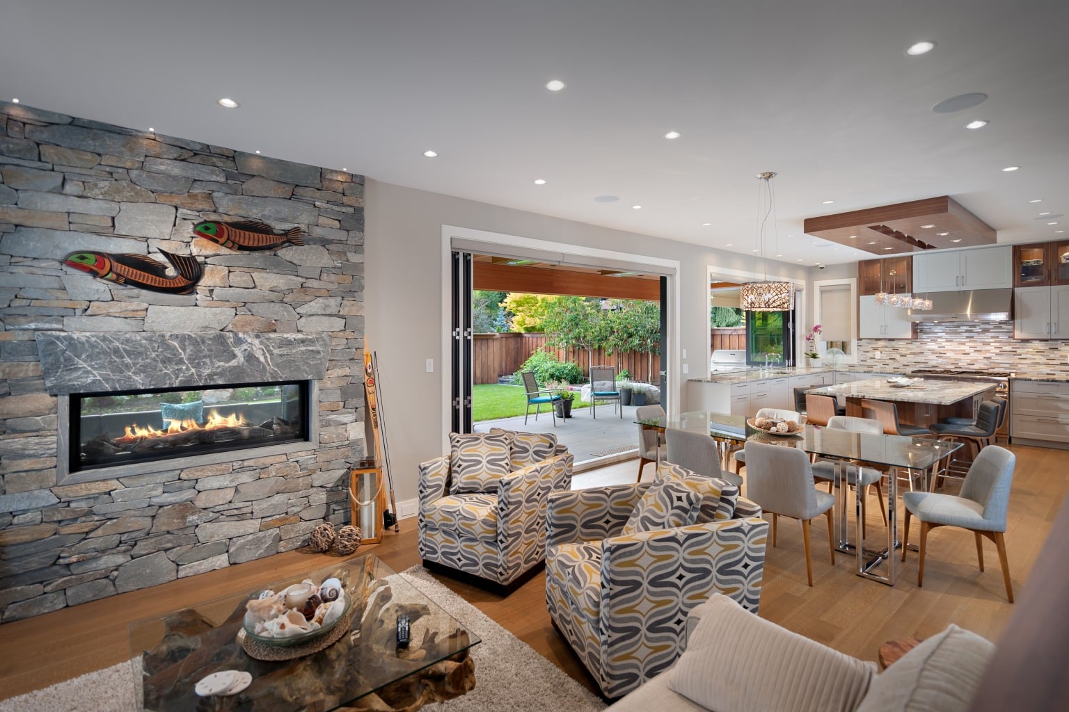 Vaulted dining and living area with exposed timber beam, stone fireplace and a glazed wall opening to a deck