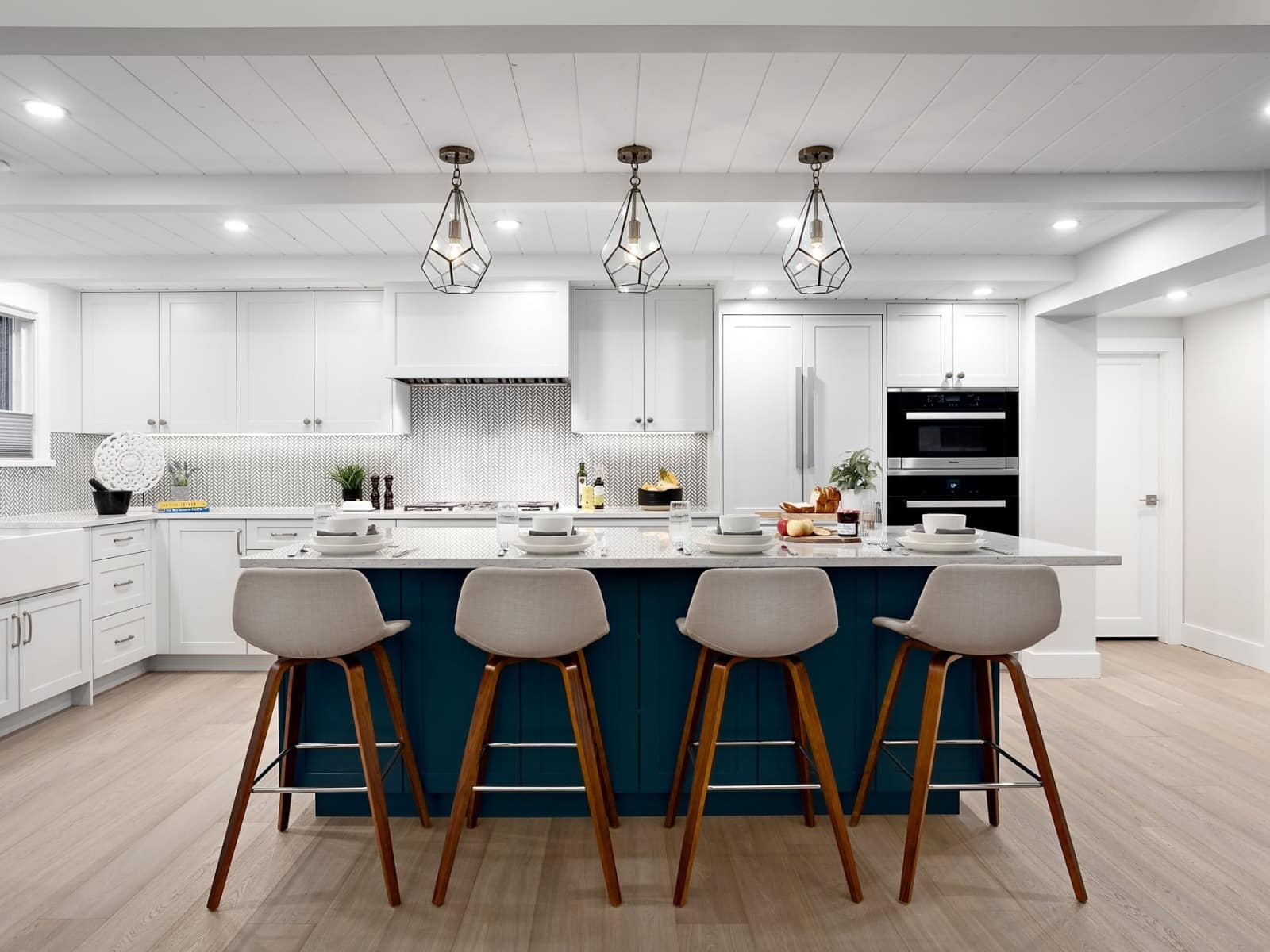 Renovated open-plan kitchen with white shaker cabinetry, teal island and herringbone tile backsplash