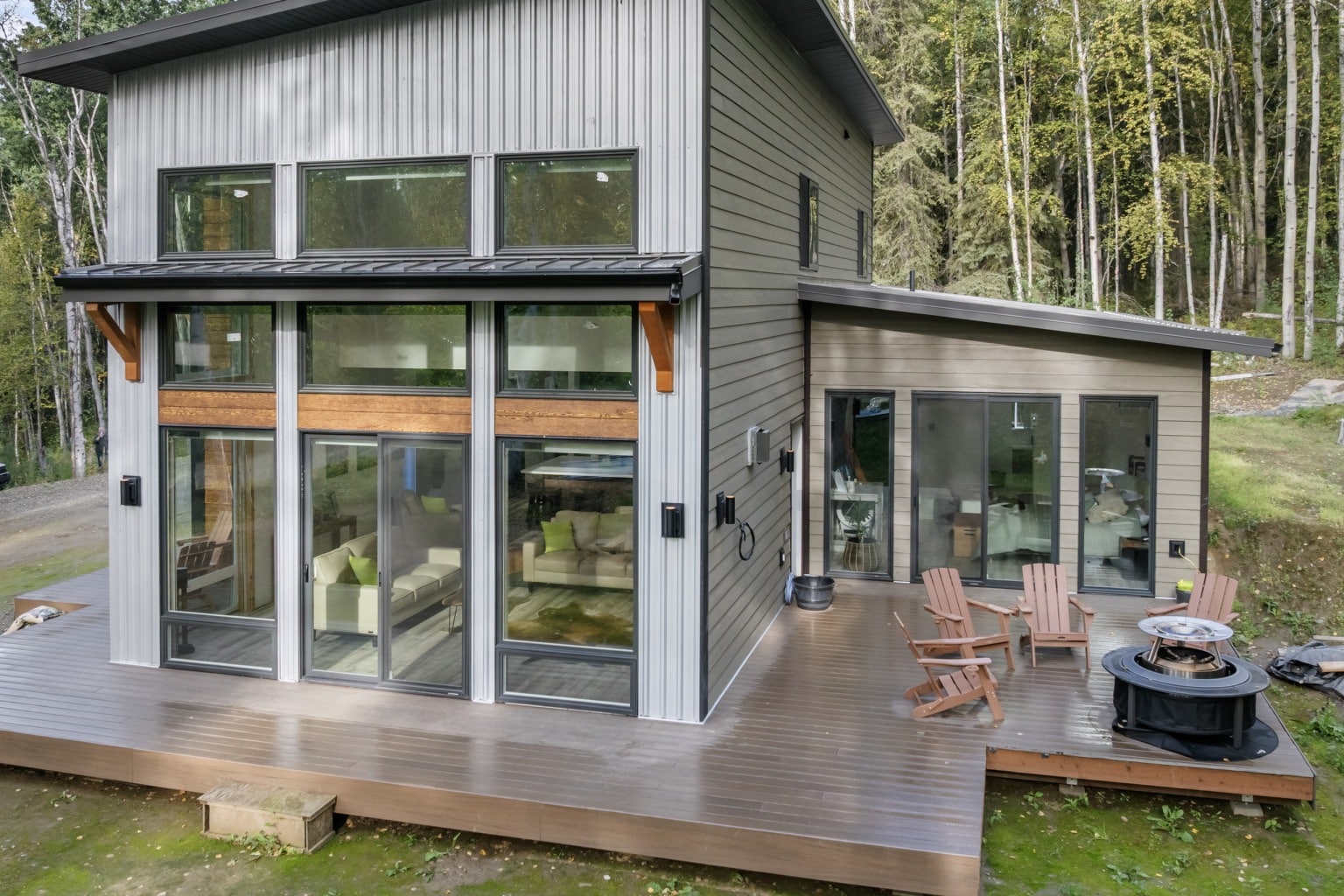A modern shed roof home with a wide deck, chairs and a fire pit at the forest edge