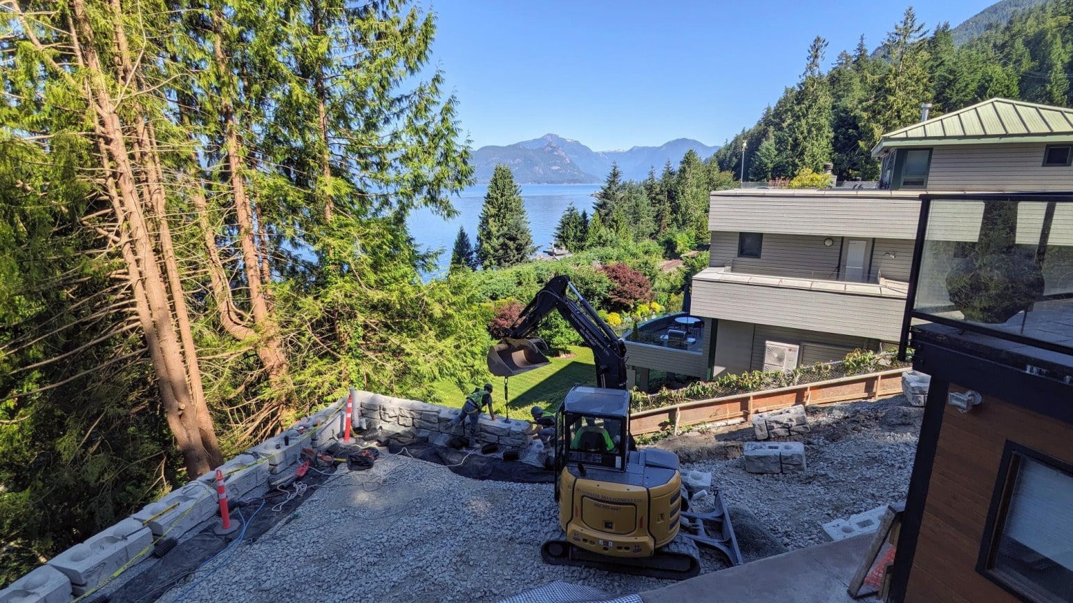 A retaining wall going in on a steep waterfront lot, with the excavator at work
