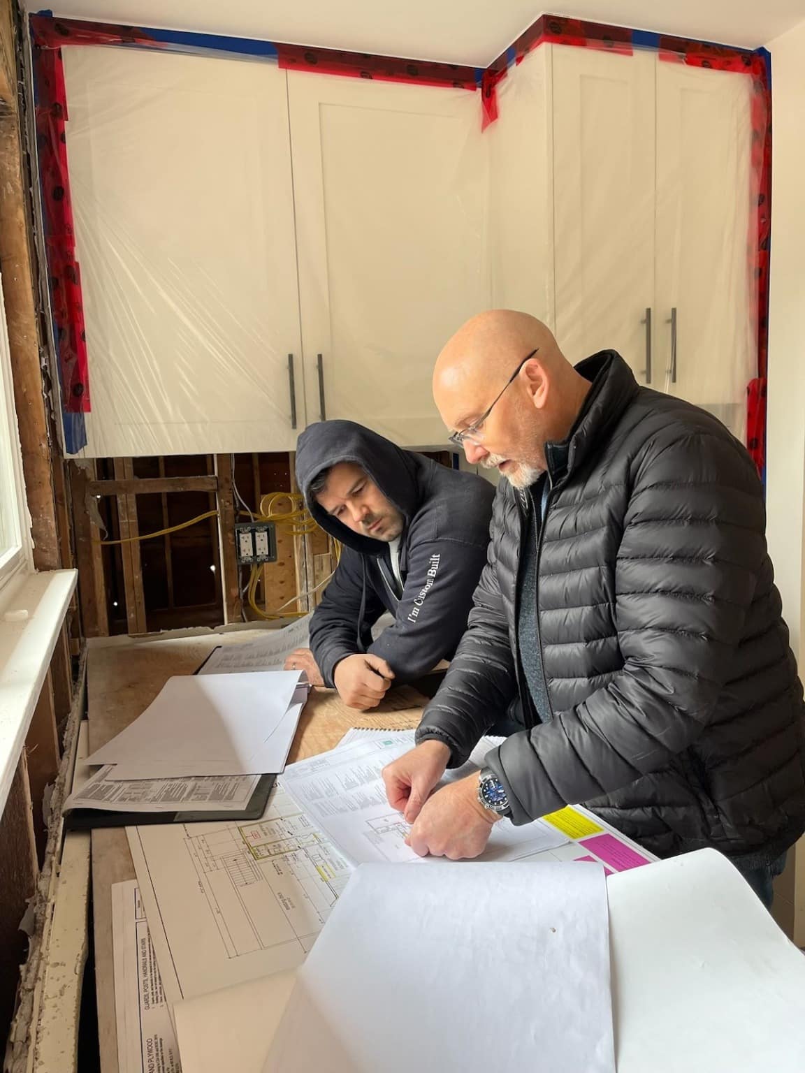 Two of the team reviewing drawings inside a kitchen stripped back for renovation
