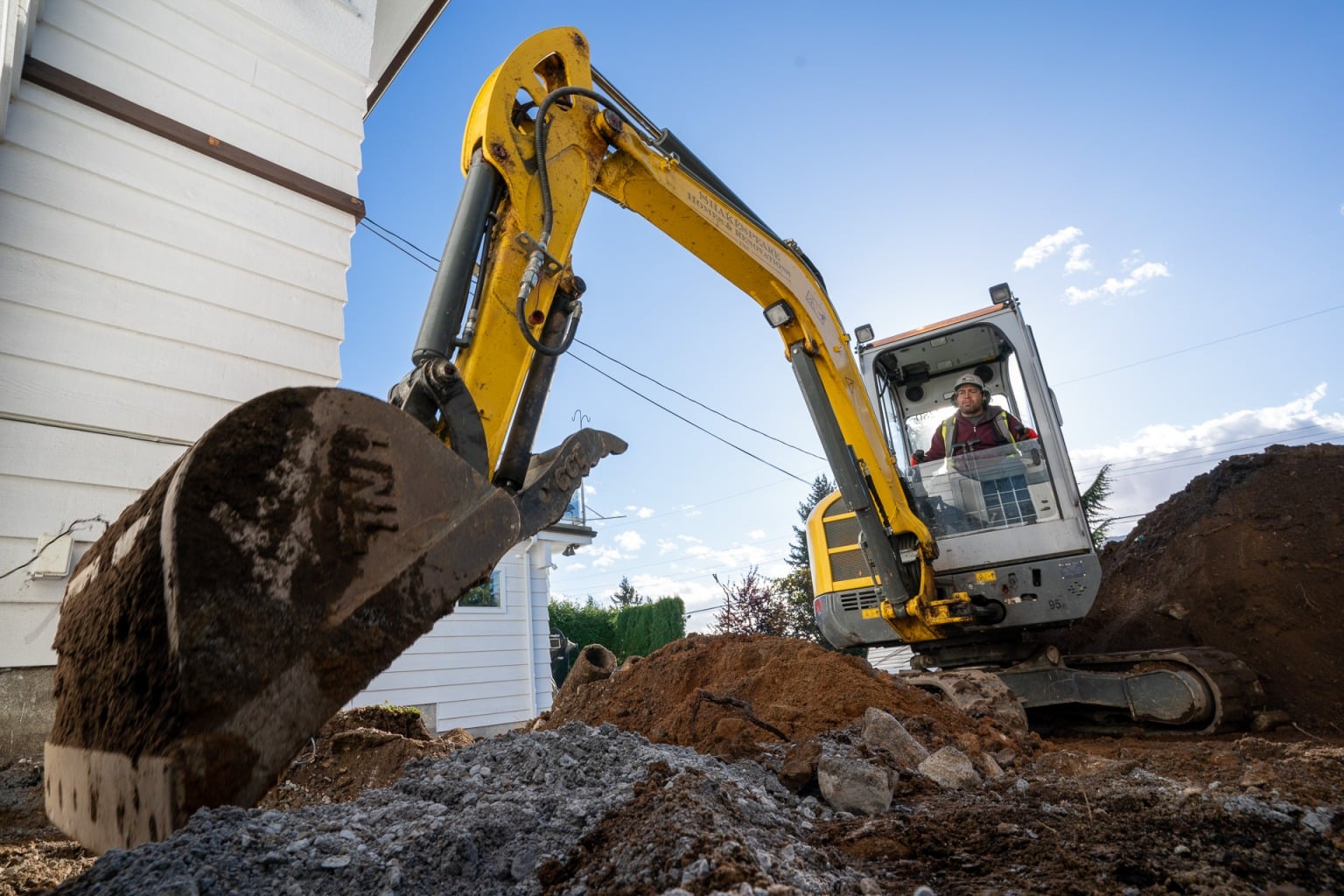 A mini excavator working beside a house on a North Vancouver site
